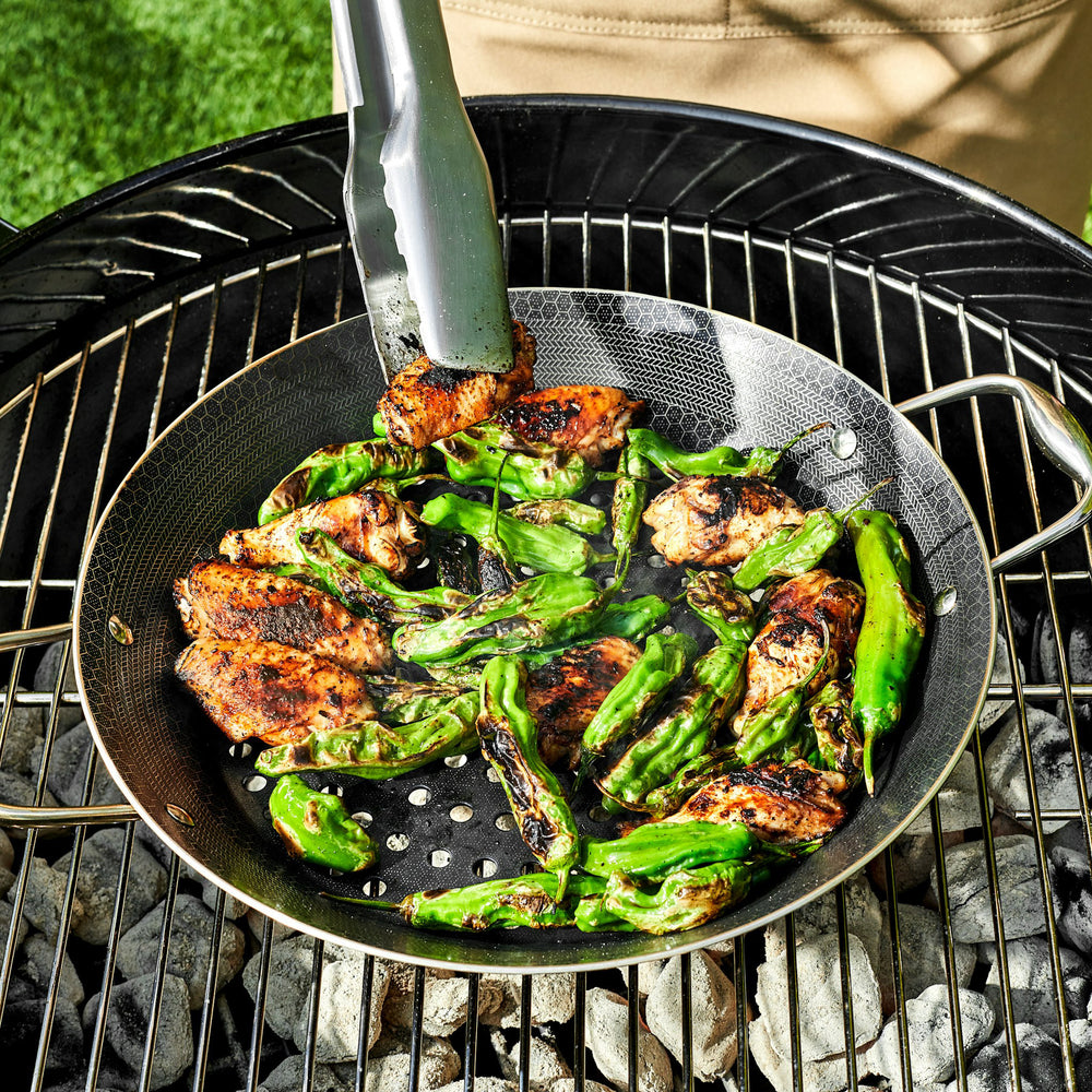 Chicken and green peppers cooking in a HexClad BBQ Grill Pan on a charcoal grill