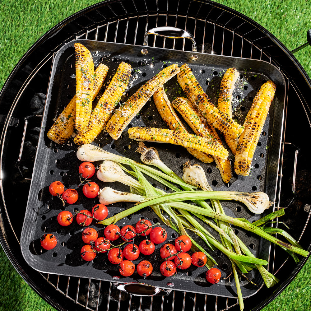 Corn, tomatoes and green onions cooking on a HexClad BBQ Grill Topper over a charcoal grill